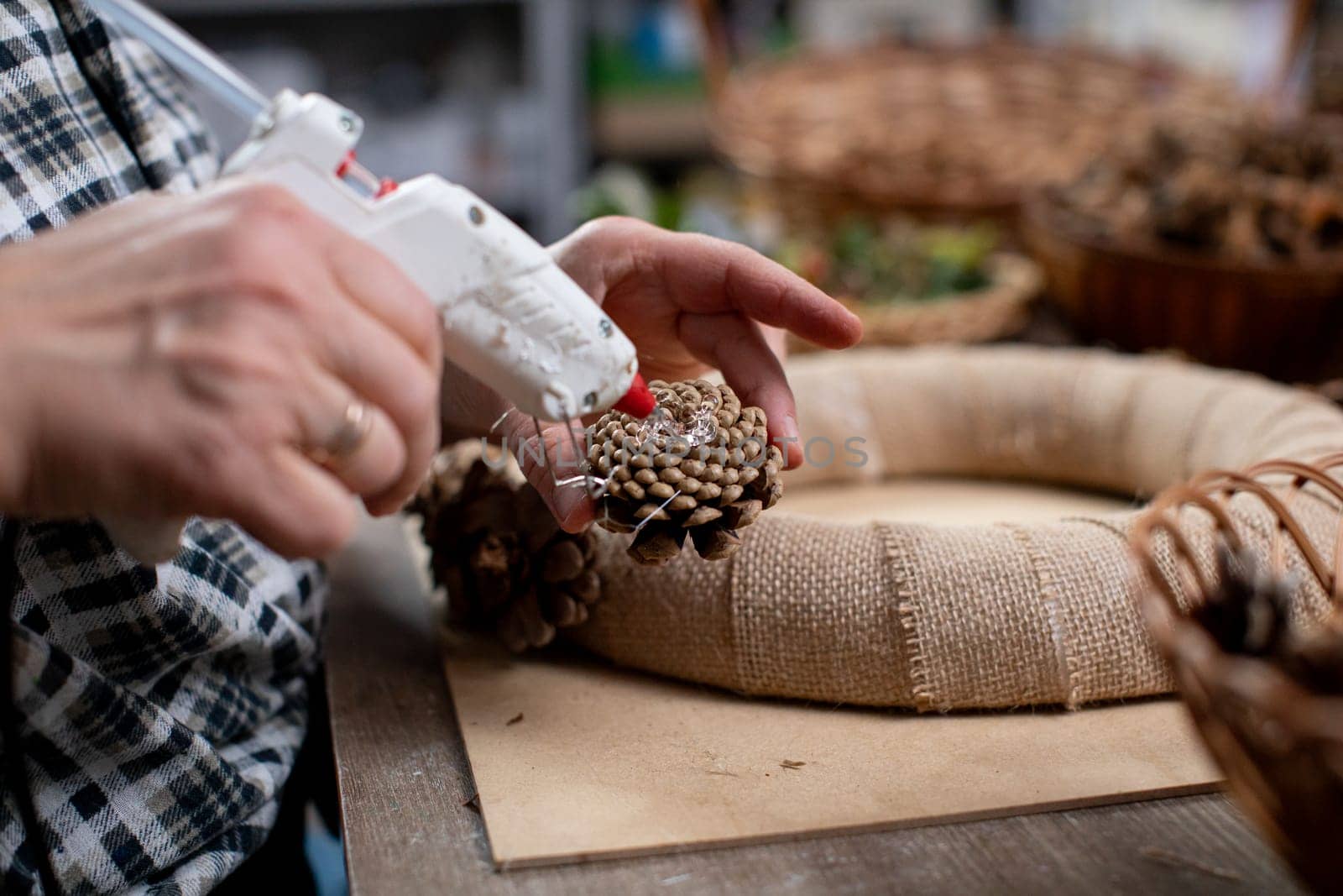 A person skillfully using a hot glue gun to attach various pinecones together for a beautiful wreath decoration