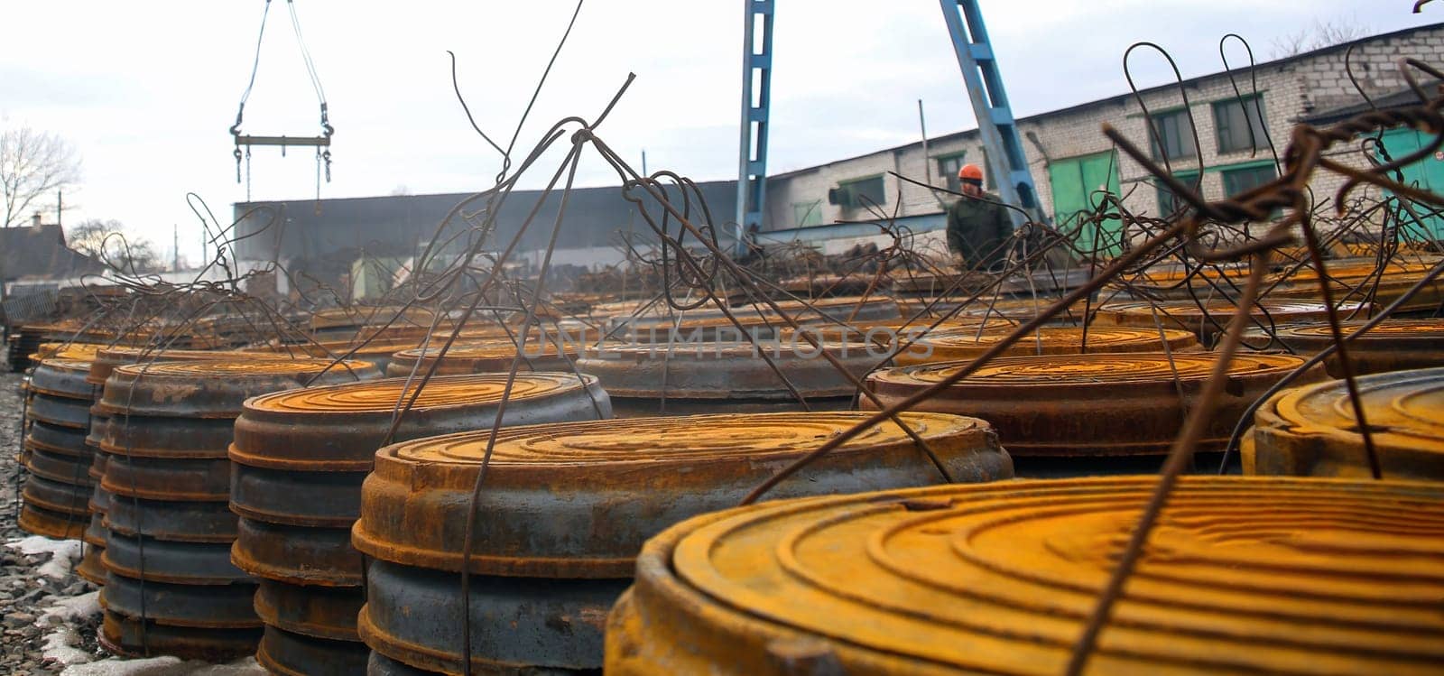 Workers are engaged in construction as a crane lifts materials over piles of stacked steel drums, indicating ongoing industrial activity during daylight.