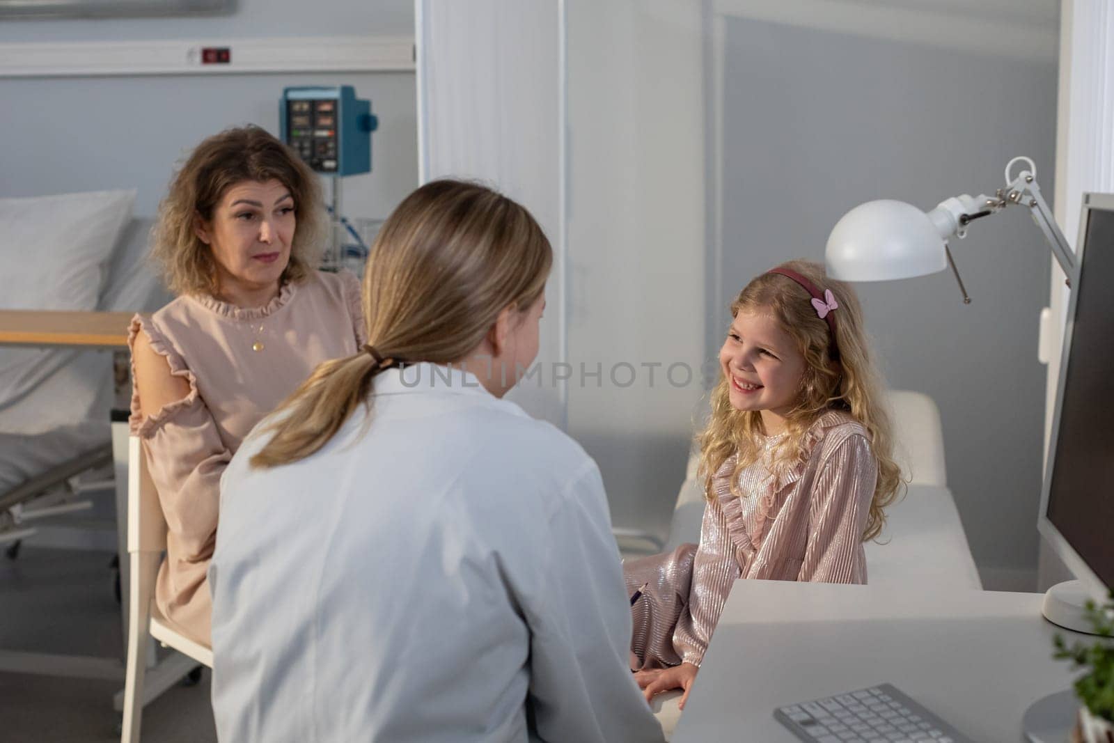 In a bright and modern clinic, a young girl is consulting with a friendly doctor accompanied by her mother