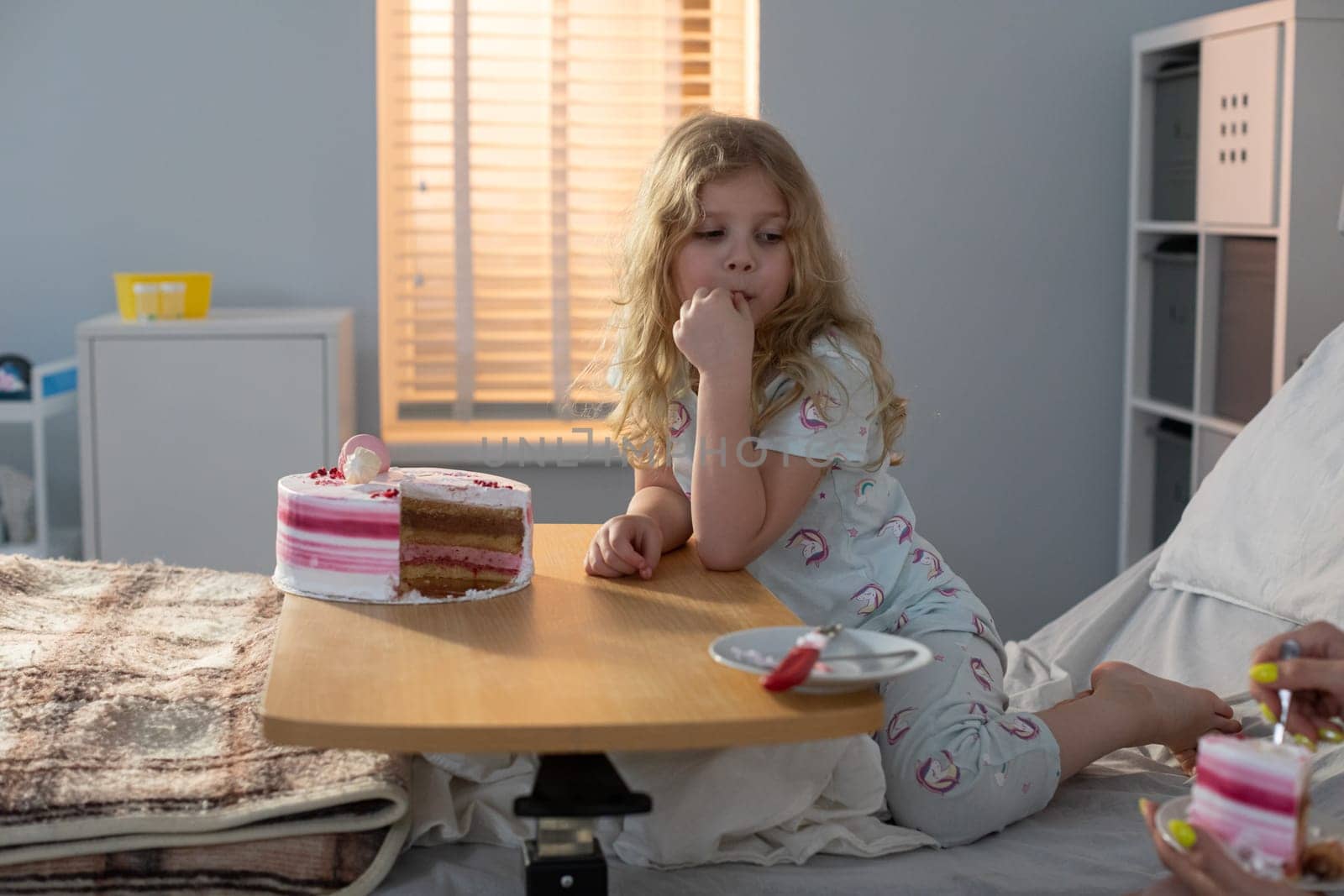 A young girl is sitting in a hospital room, thoughtfully enjoying a delightful snack served on a meal tray