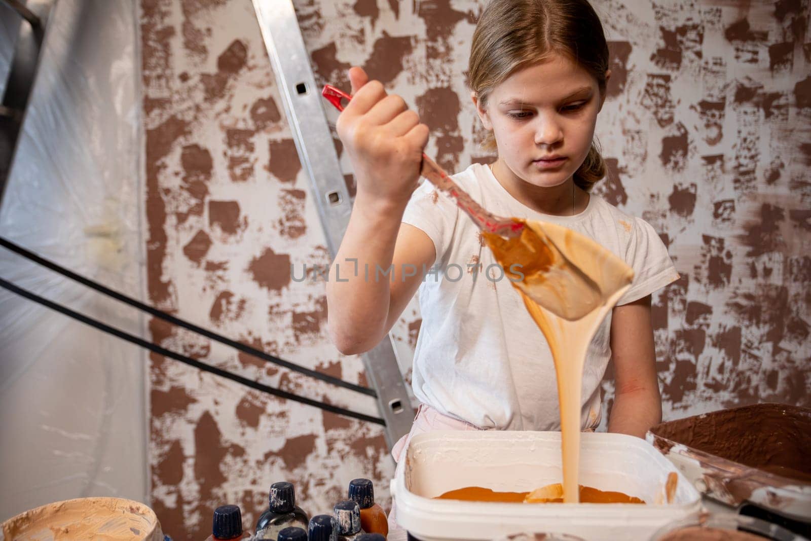 A young girl is actively and creatively mixing orange paint, beautifully capturing the essence of childhood artistry