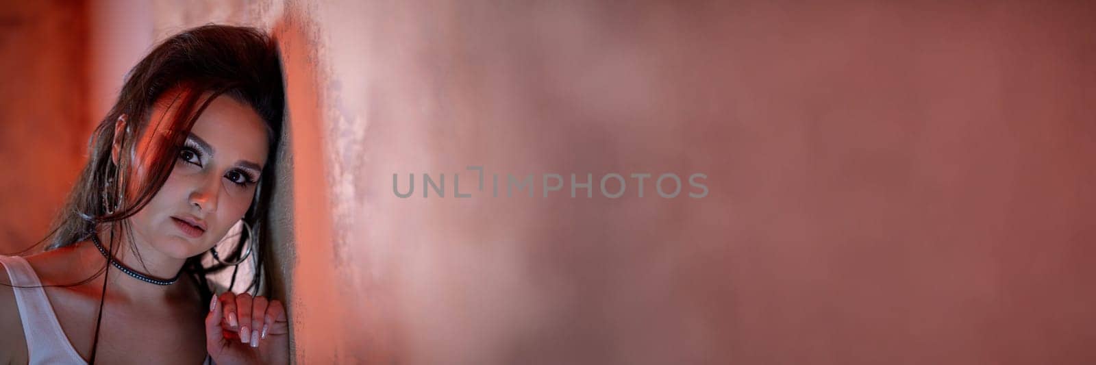 A moody portrait of a stunningly beautiful young woman with flowing hair, leaning against a textured wall