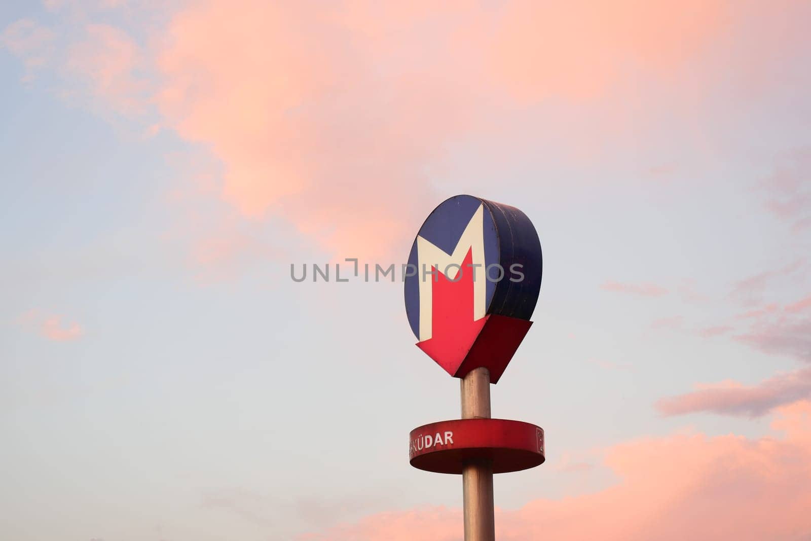 A subway station sign stands tall with a pastel sky at dusk.