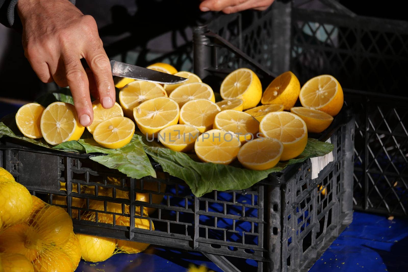 Hands slice vibrant lemons on a green leaf in a bustling market.