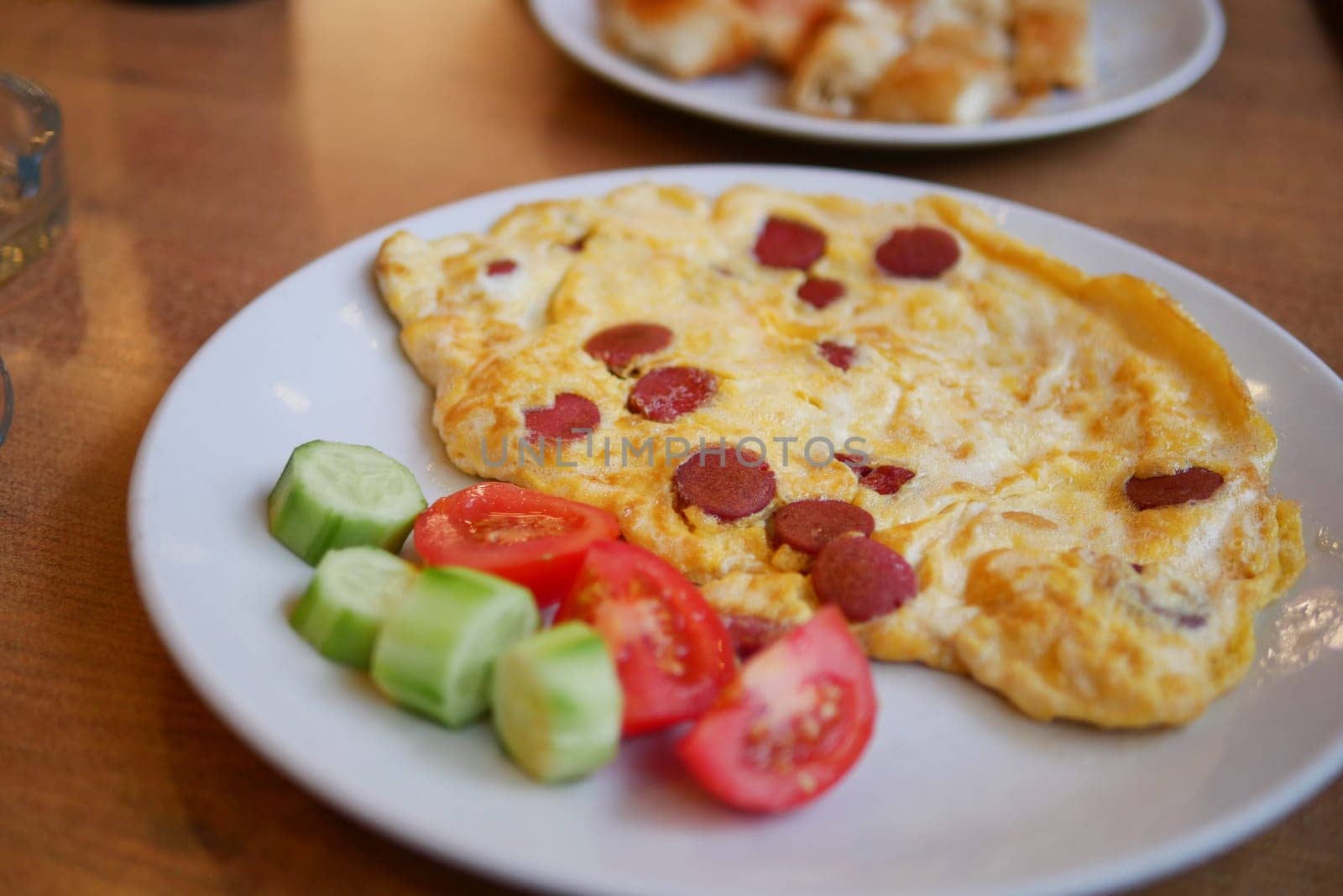 Omelet with sliced sausage served with fresh tomato and cucumber slices.