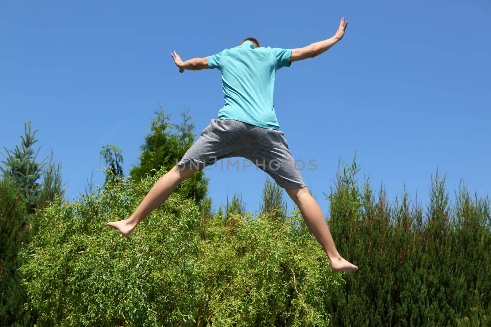 A young boy leaps joyfully high in the air over a vibrant, lush green garden, radiating a true sense of joy