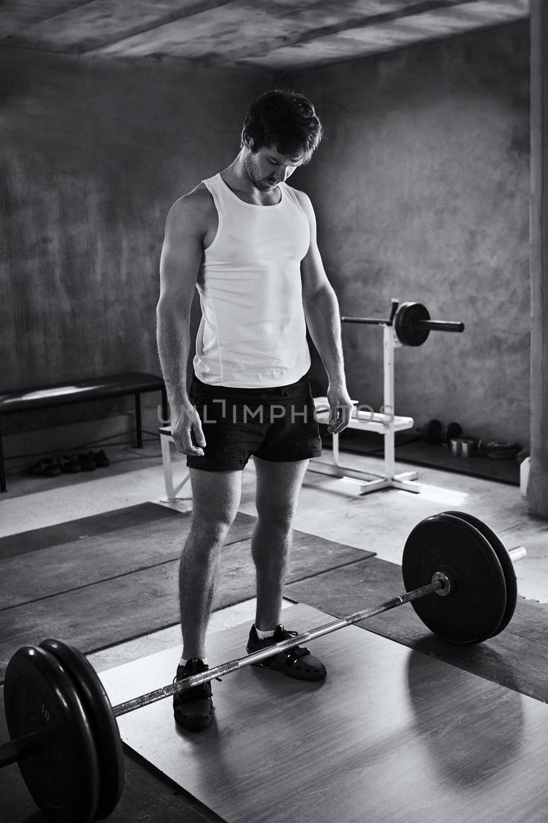 Black and white image of a strong young man looking quietly at the weights he is about to lift