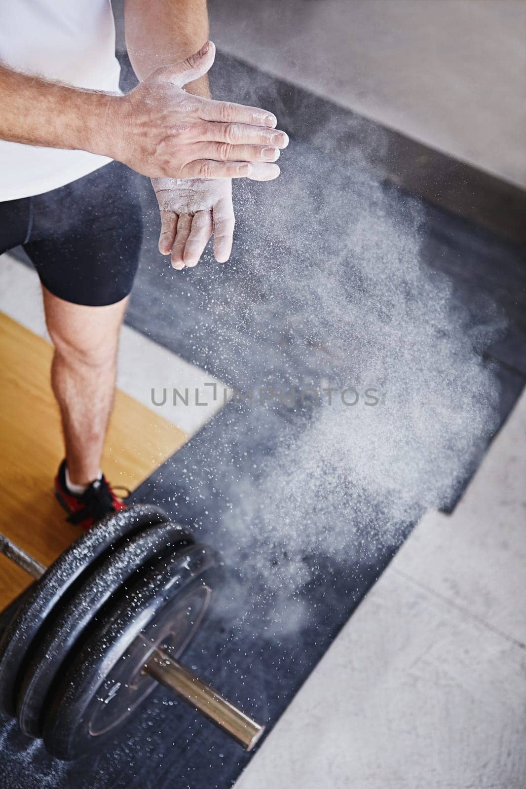 High angle view of a man dusting his hands with powder with the weight he's about to lift at his feet