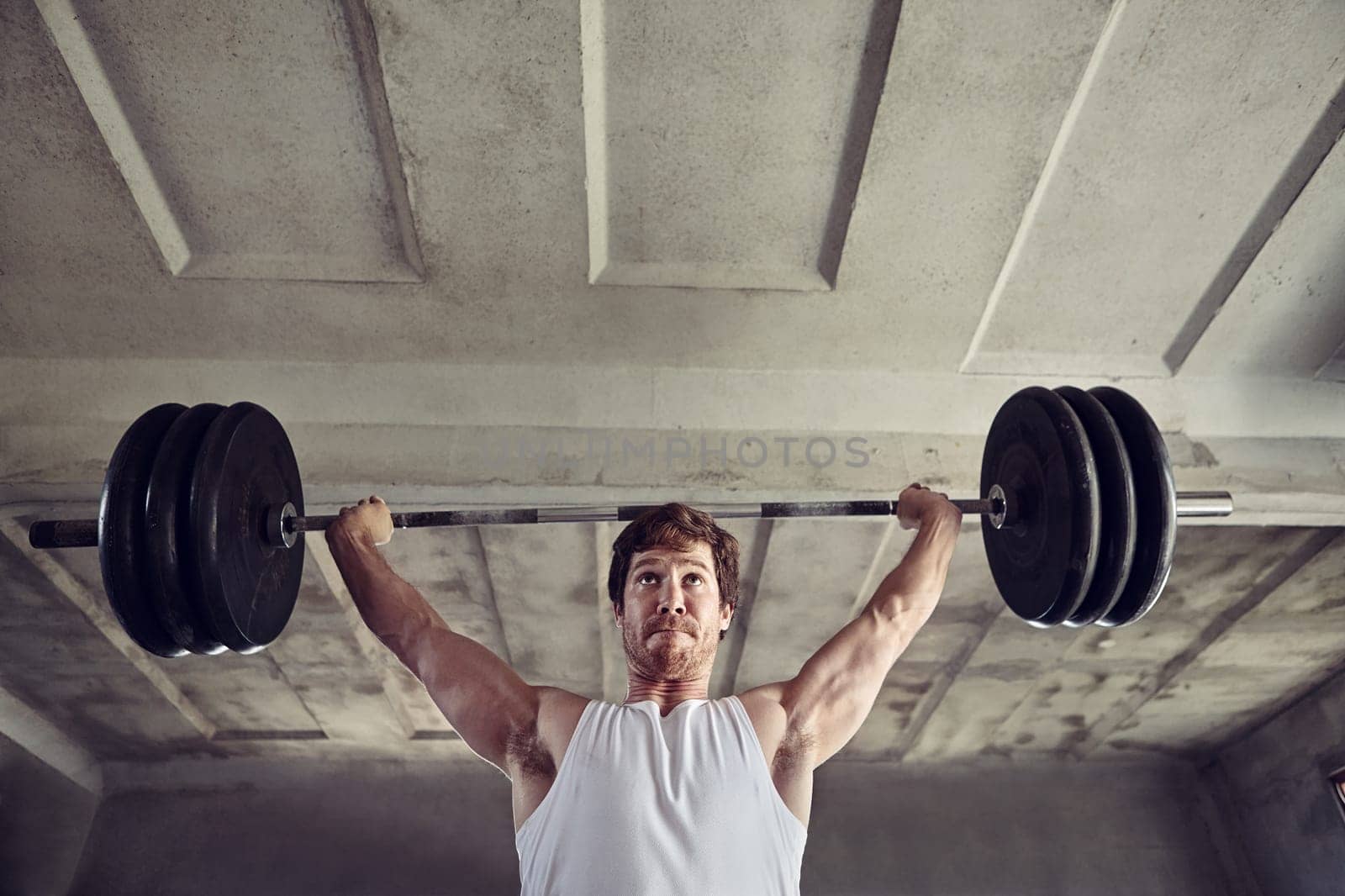 Low angle shot of a strong young man lifting heavy weigths above his head with a determined expression