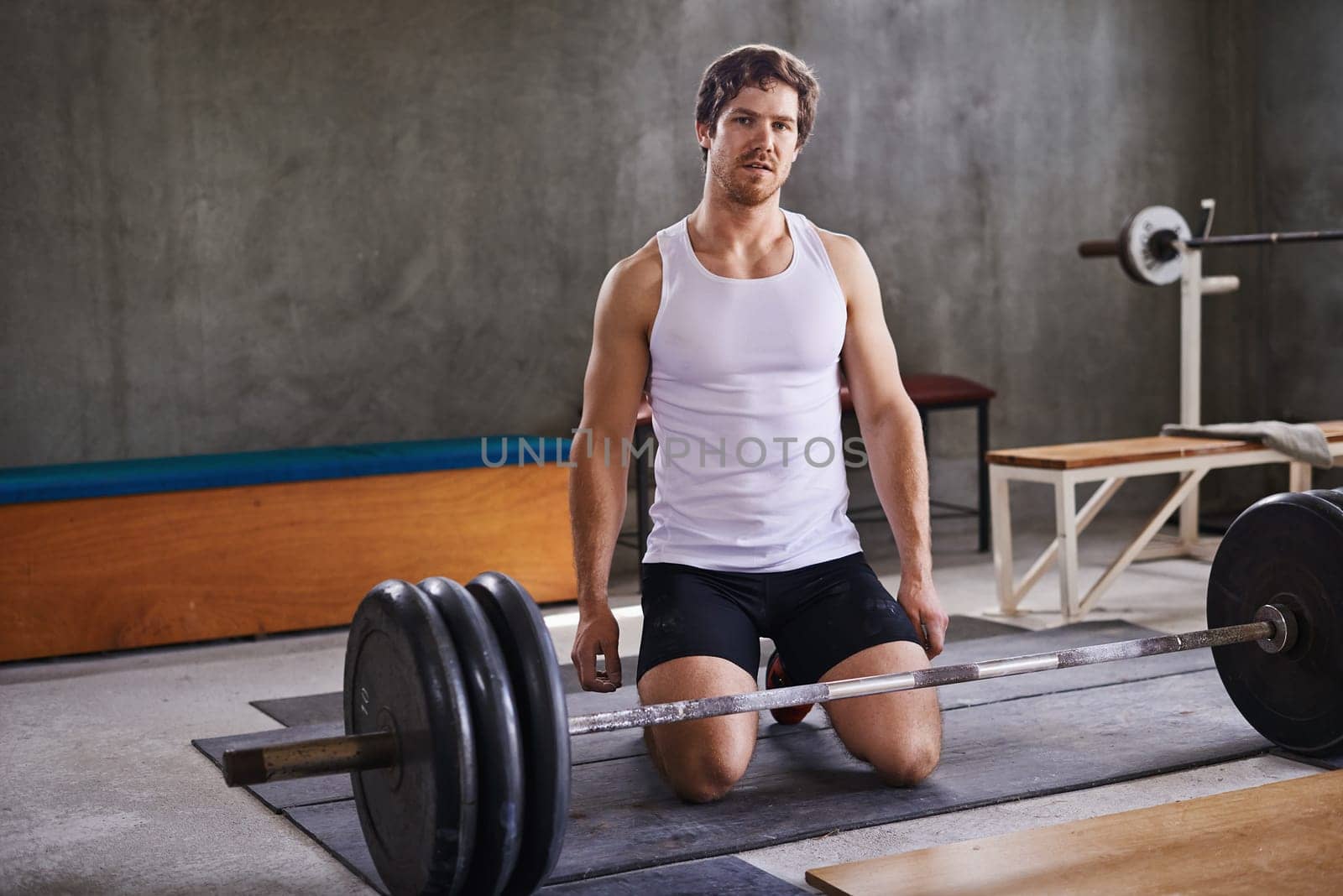 Fit personal trainer kneeling behind his weightlifting equipment in a private gym