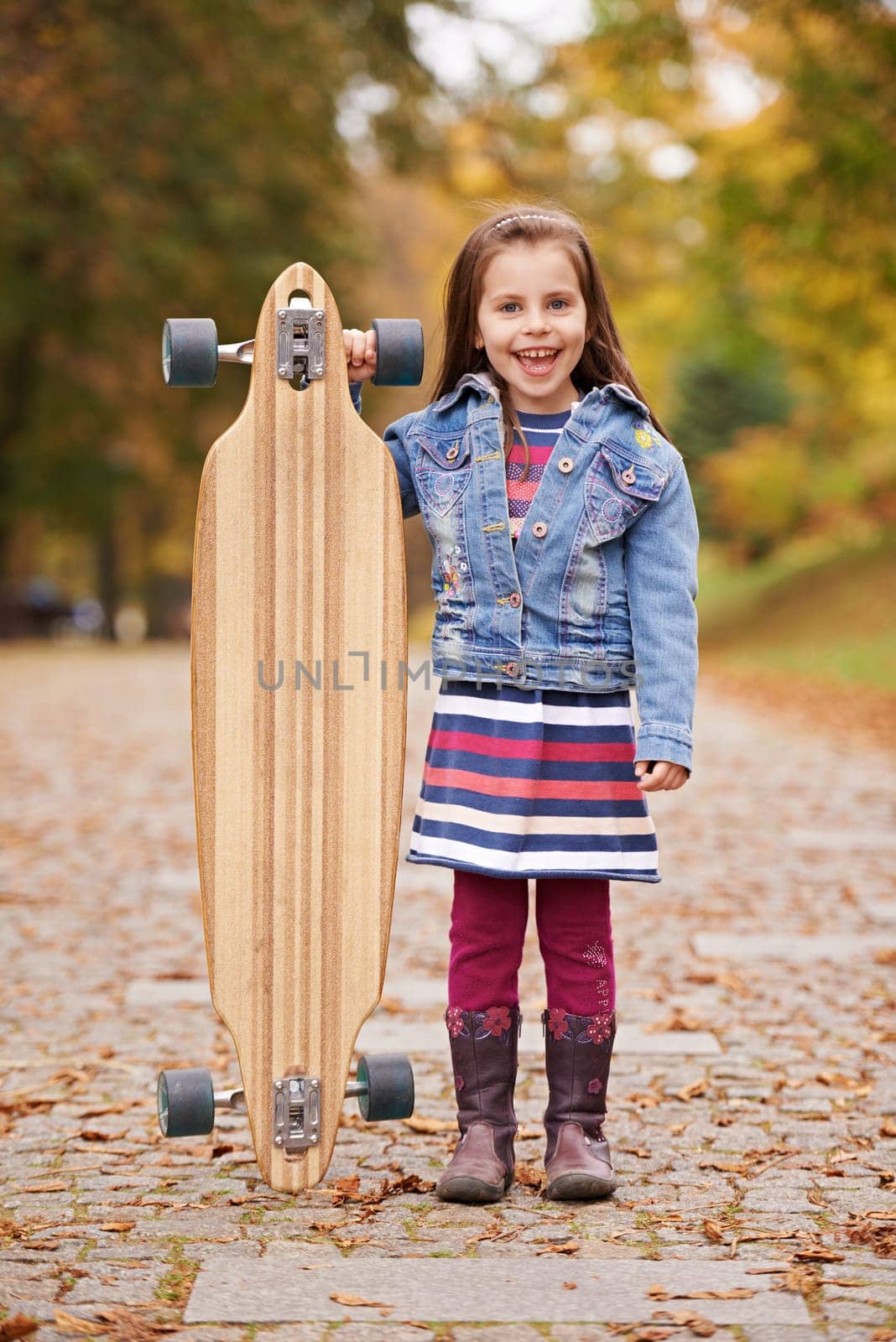 Cute little girl standing alongside a longboard skate board outdoors