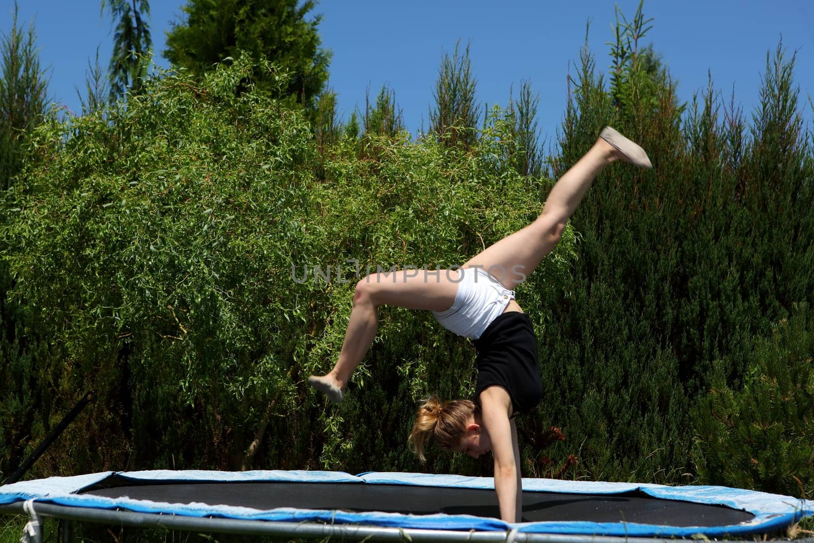 A young girl joyfully displays her acrobatic skills on a trampoline, surrounded by vibrant lush greenery
