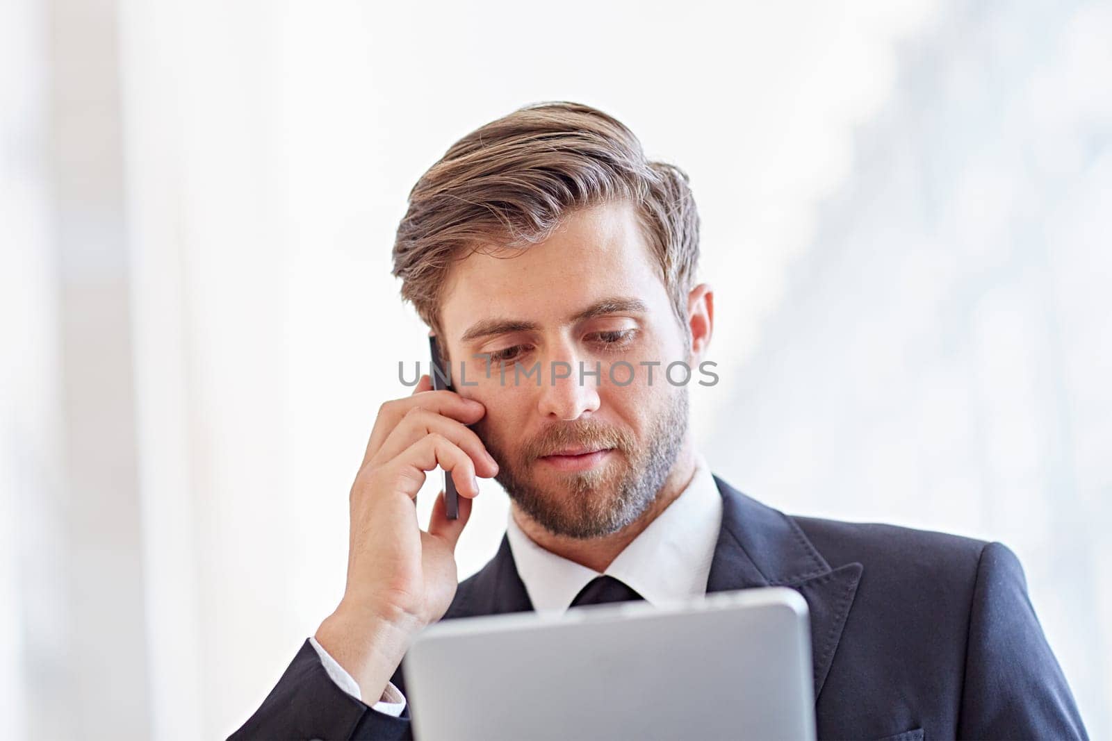 Closeup of a serious corporate executive listening on his phone while looking at a digital tablet