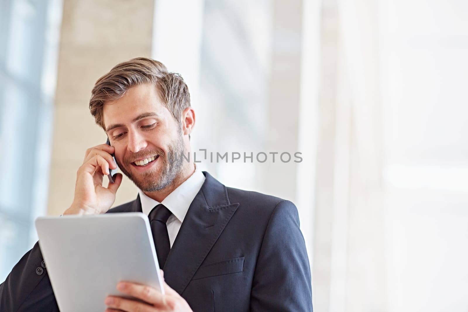 Corporate executive smiling while talking on his phone and looking at a digital tablet