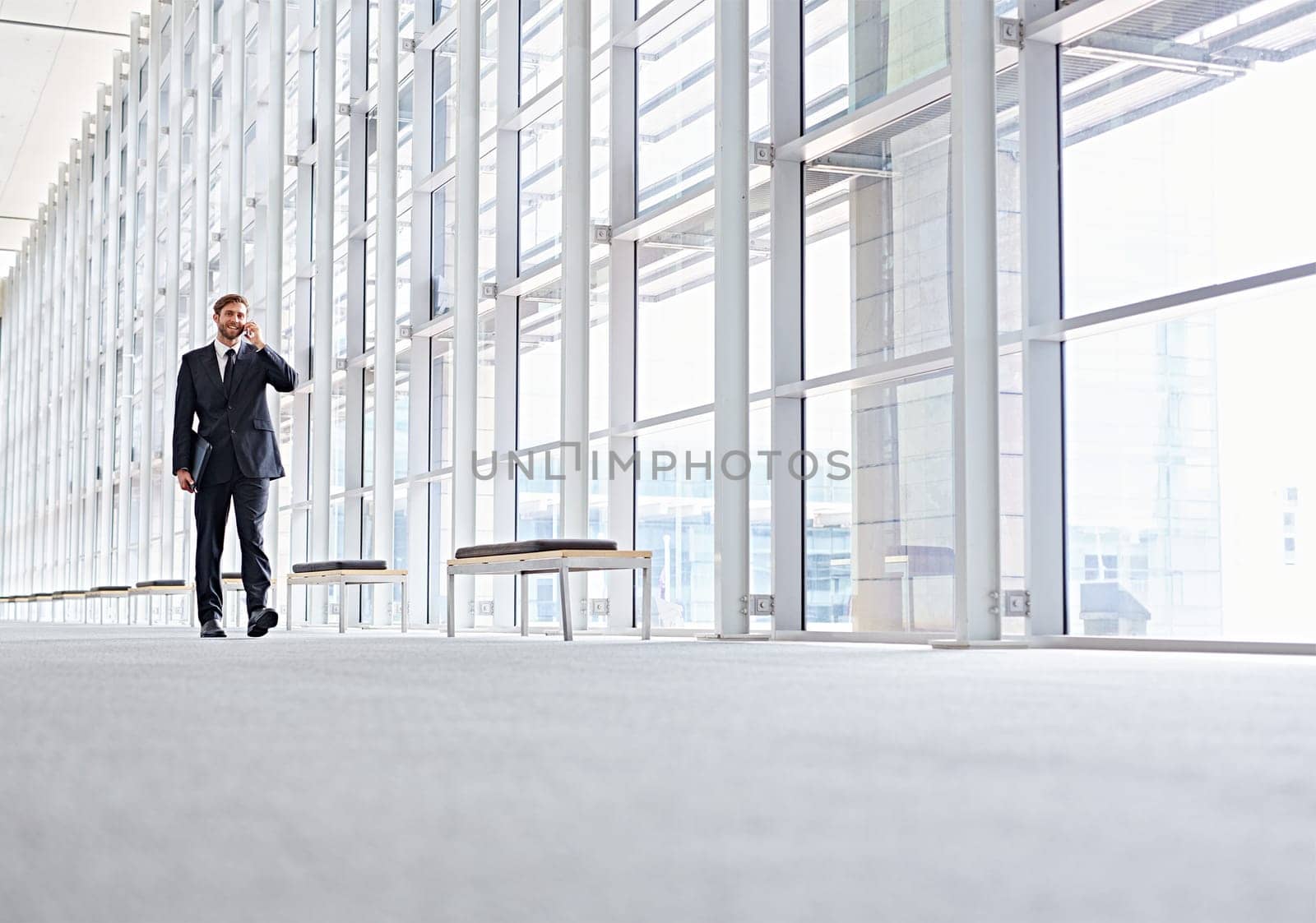 Low angle shot of a corporate executive walking along a modern corridor talking on his mobile phone