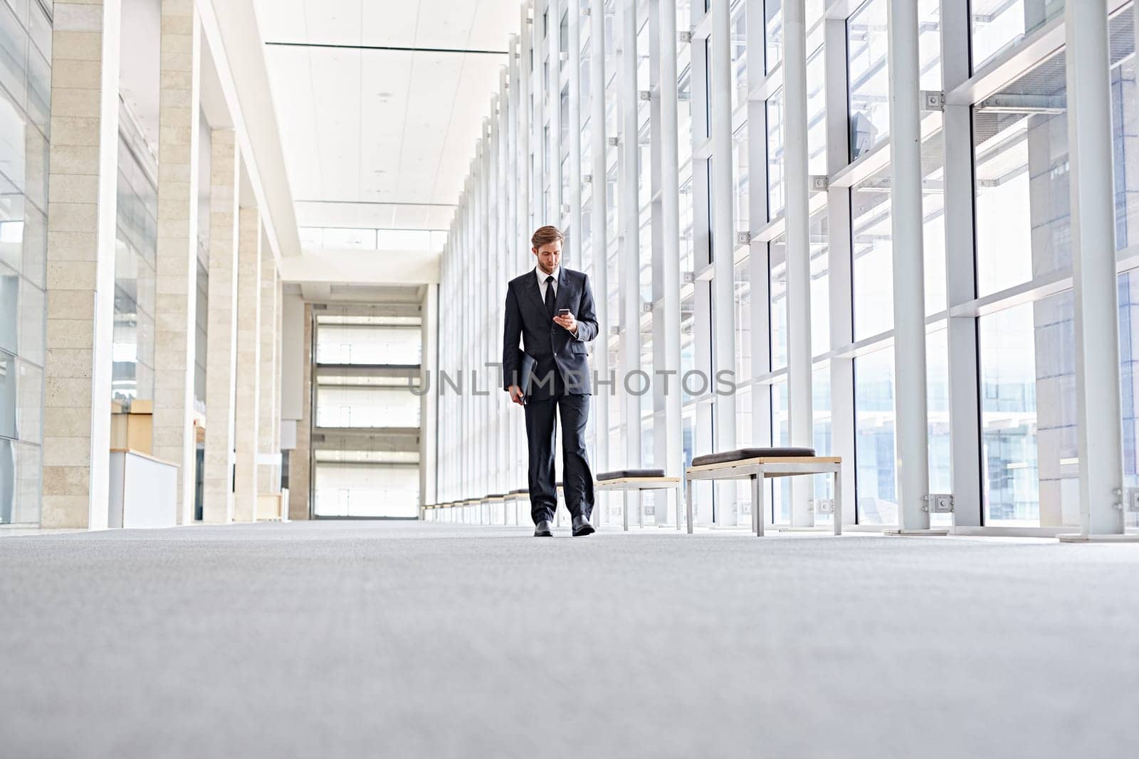 Low angle shot of a corporate executive walking along a modern corridor while using his mobile phone