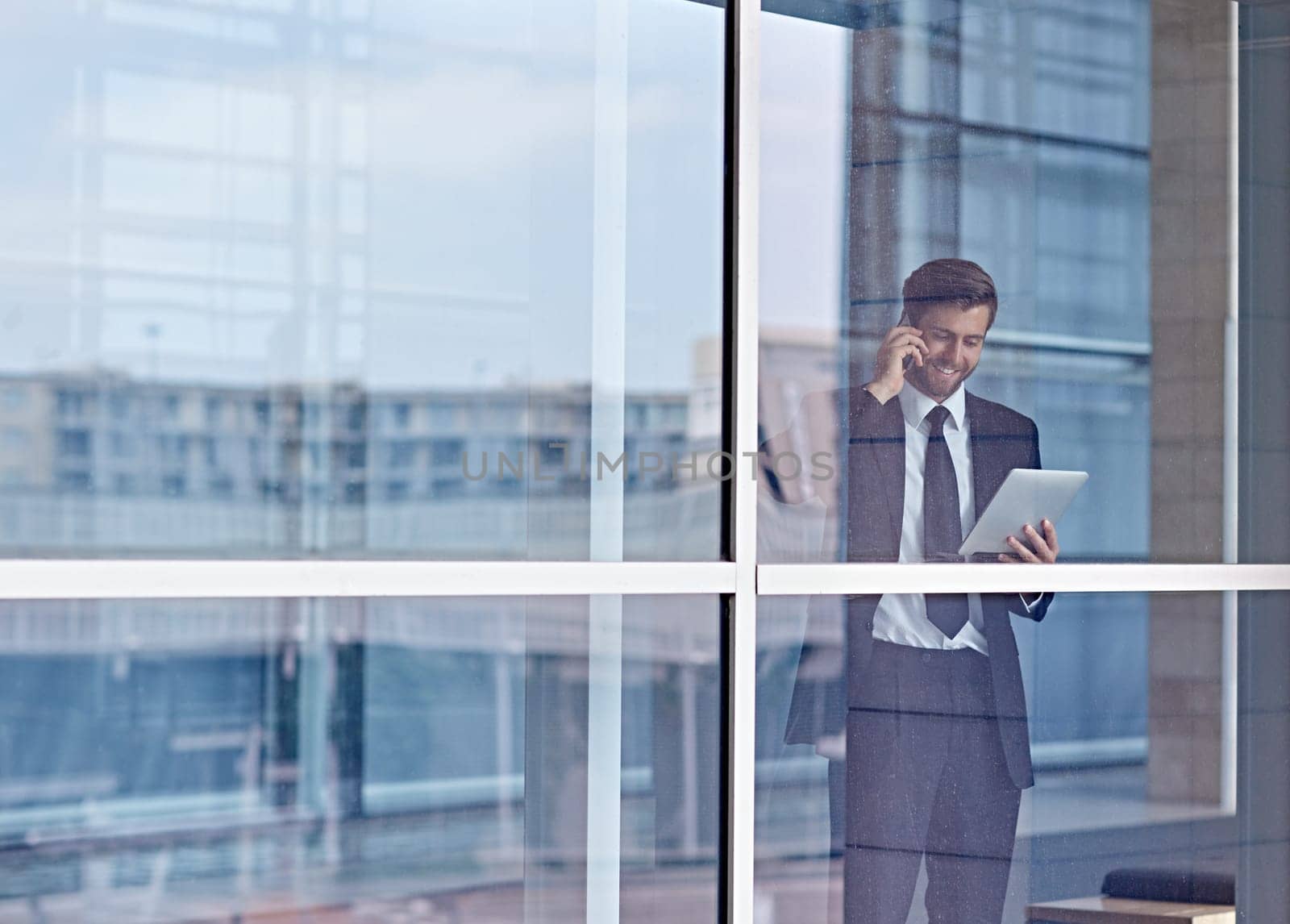 View through a window of a corporate executive talking on his phone and looking at a digital tablet