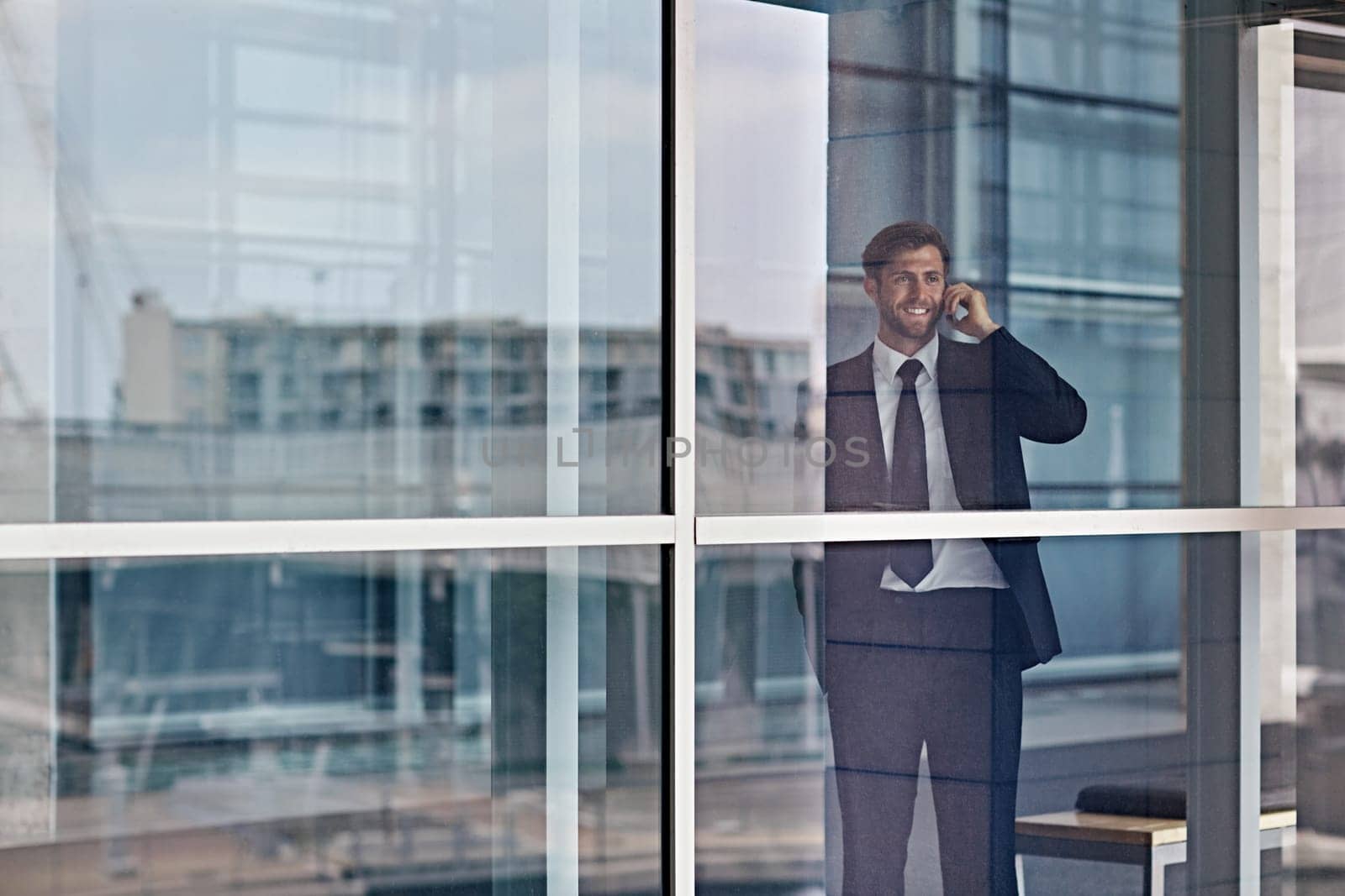 A happy businessman looking out the window while talking on his cellphone