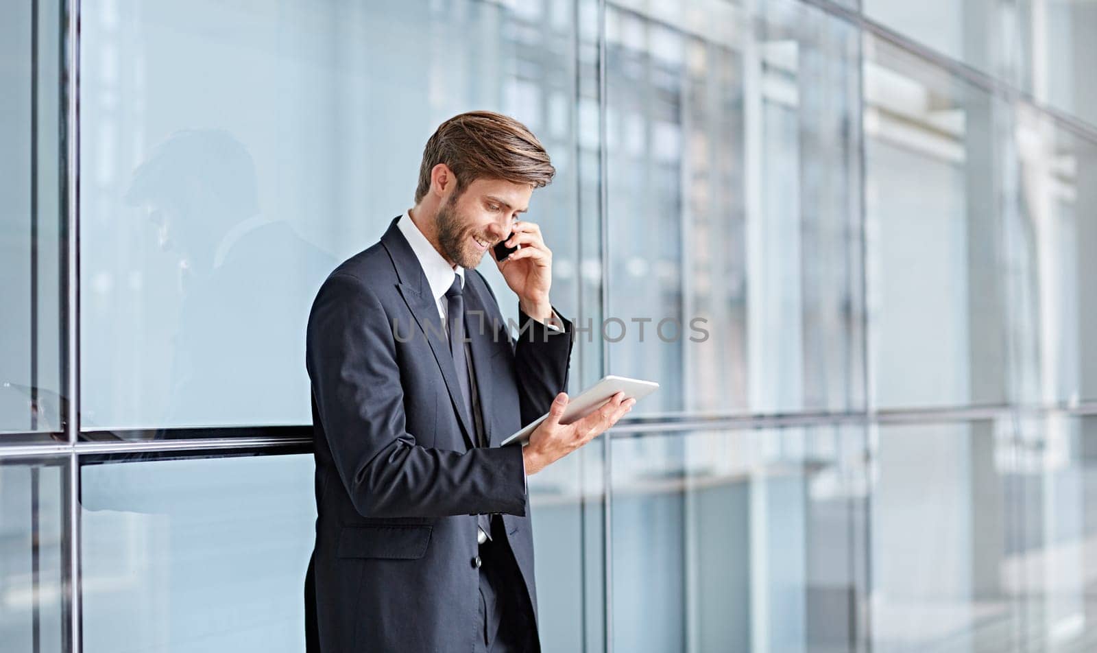 Corporate executive smiling while talking on his phone and looking at a digital tablet