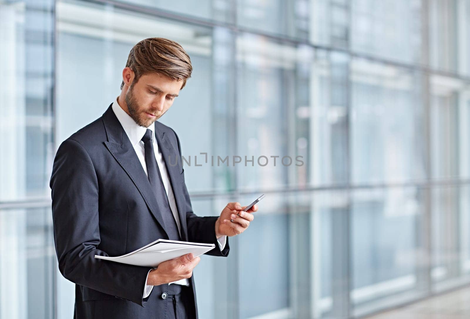 Corporate executive holding his cell phone in a modern architectural setting while looking at notes