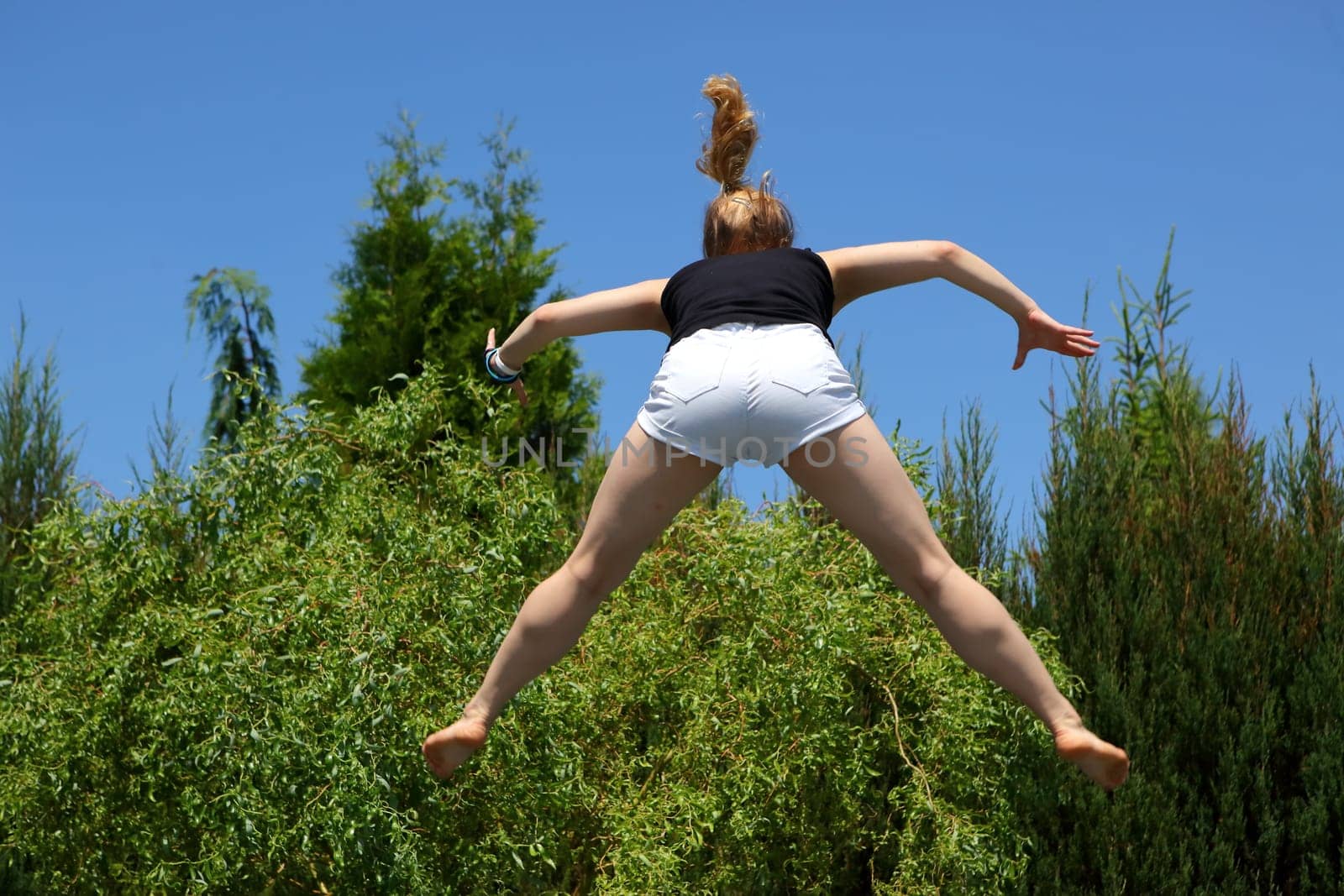 A young person joyfully leaping high into the air, surrounded by lush greenery and bright blue, sunny skies