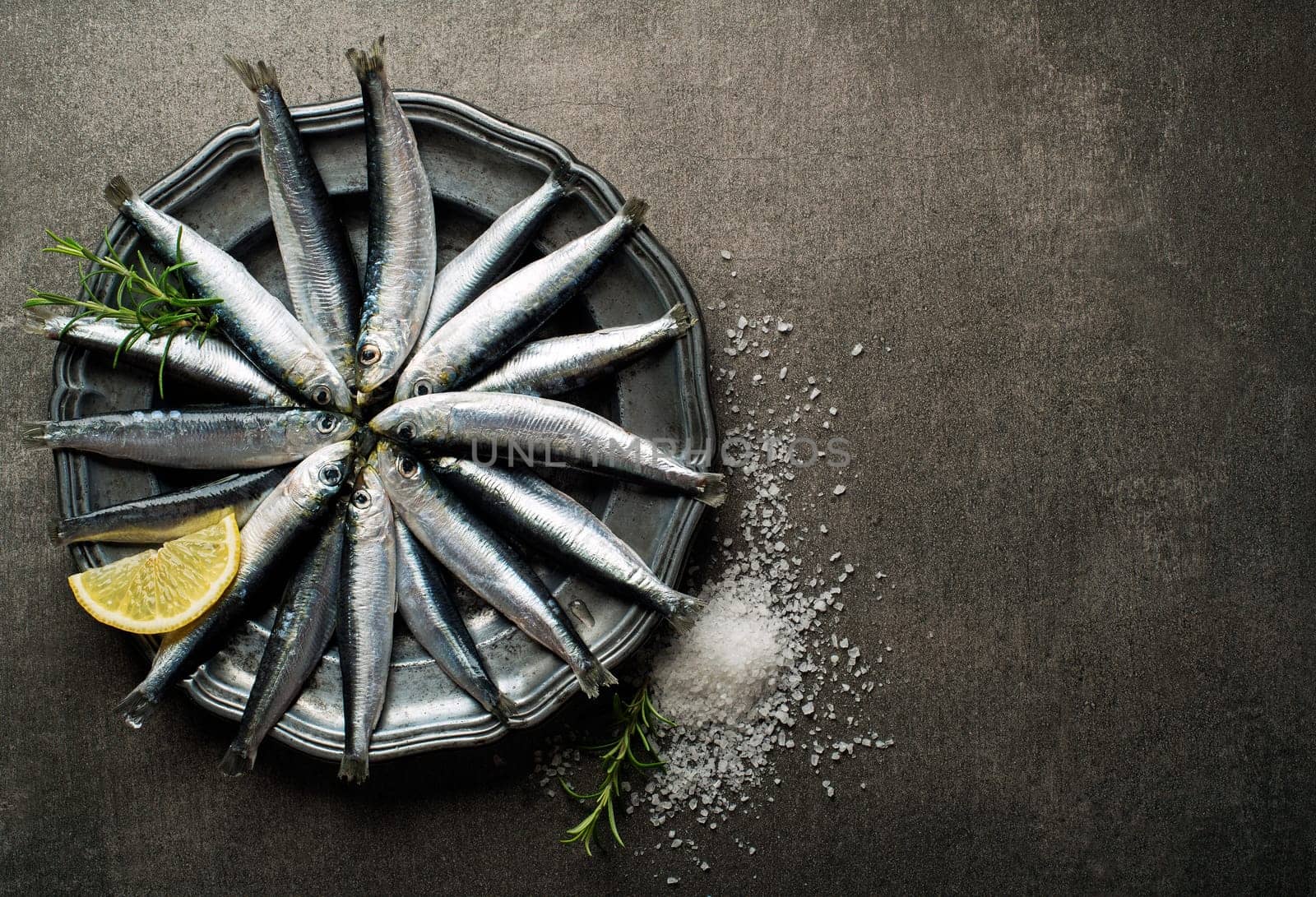 Fresh raw sardines with salt and herbs on rustic background