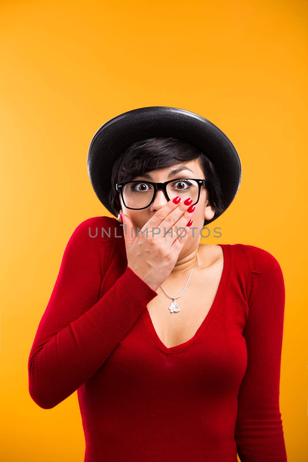 Beautiful nerd girl wearing a santa hat and holding a gift, against yellow background