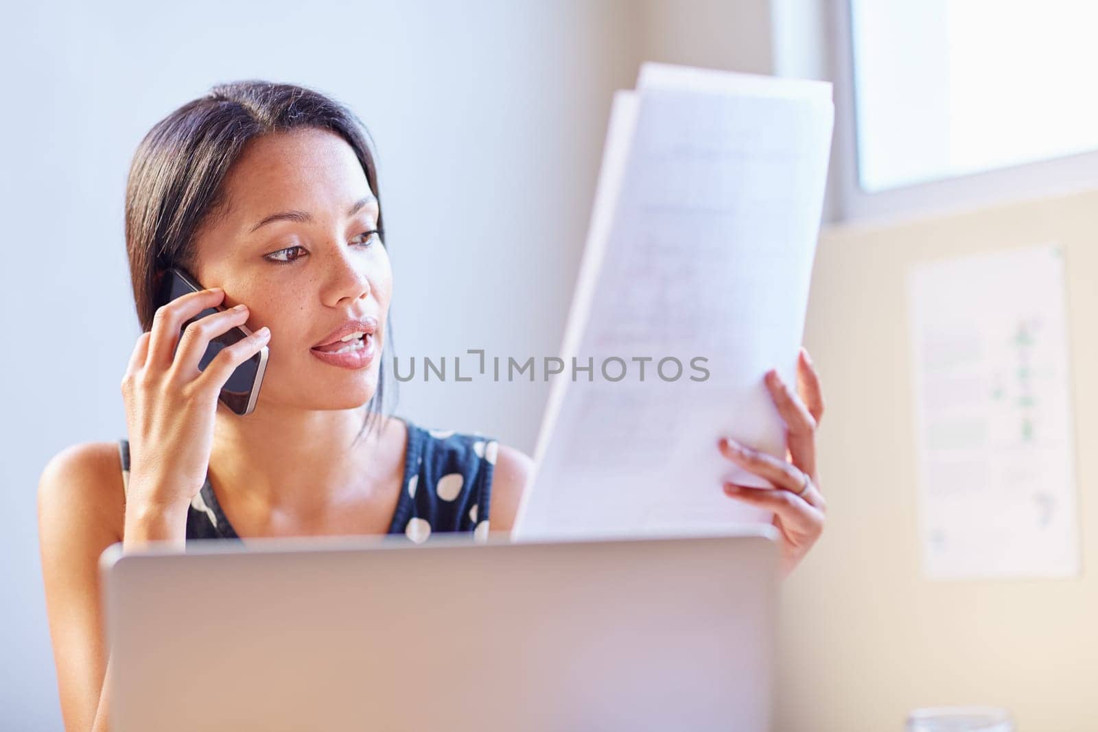 A young businesswoman talking on the phone while looking at a document