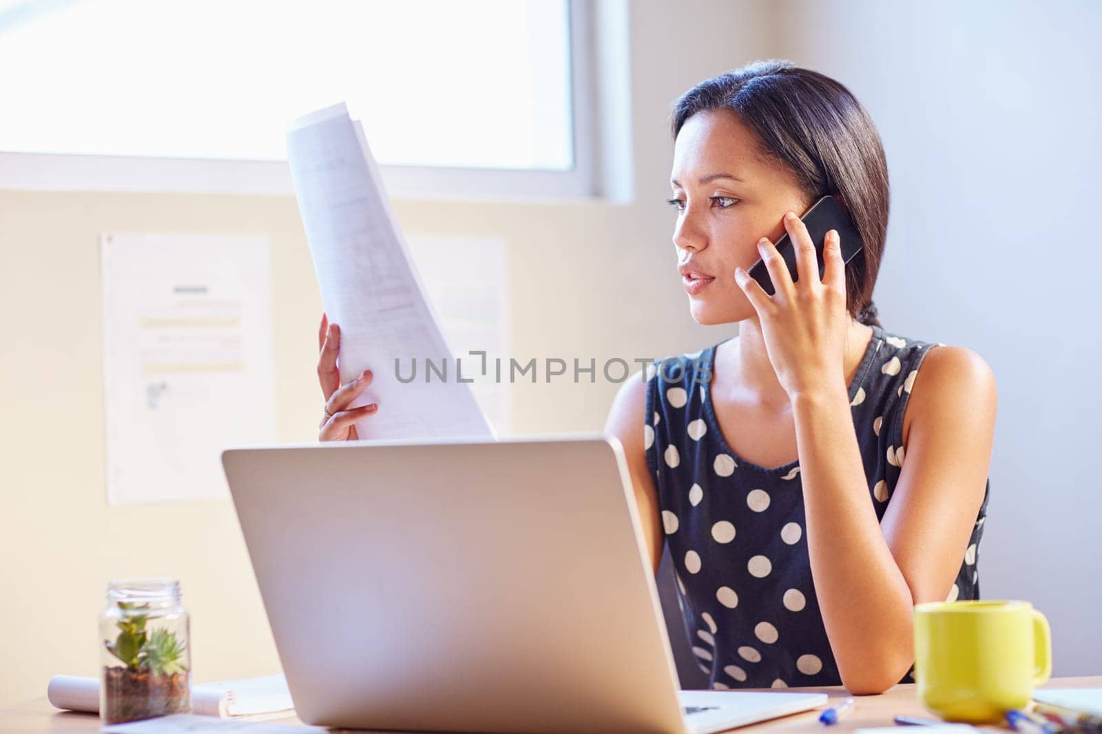 A young businesswoman talking on the phone while looking at a document