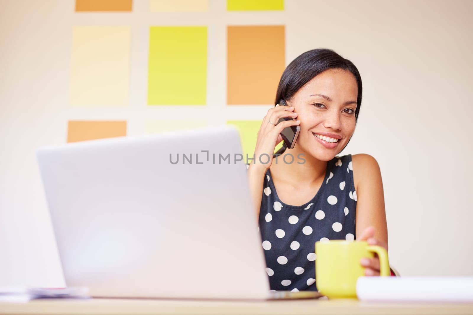 A young businesswoman talking on the phone while sitting in front of her laptop