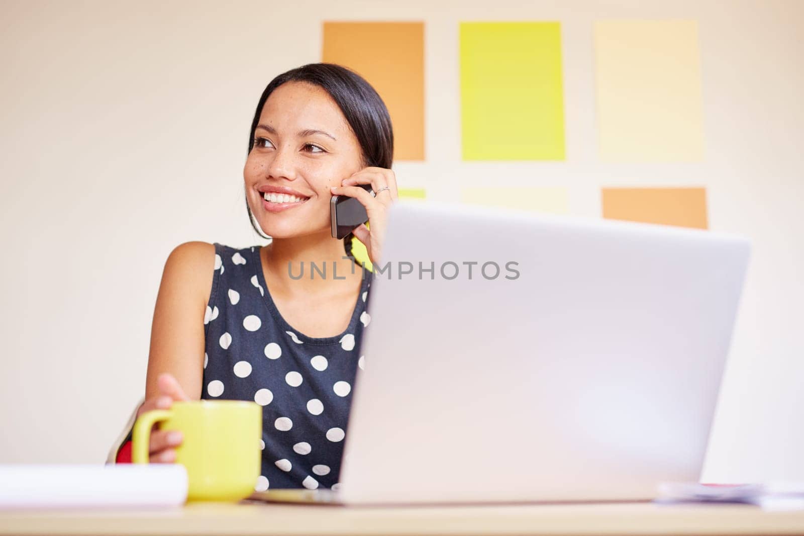 A young businesswoman talking on the phone while sitting in front of her laptop