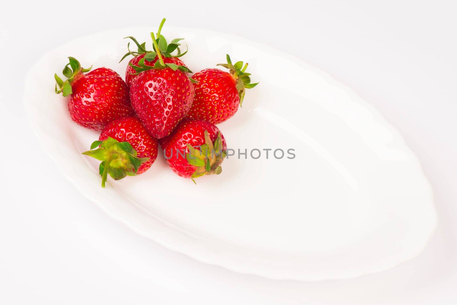 Fresh raw ripe organic strawberries are on white plate on white background.