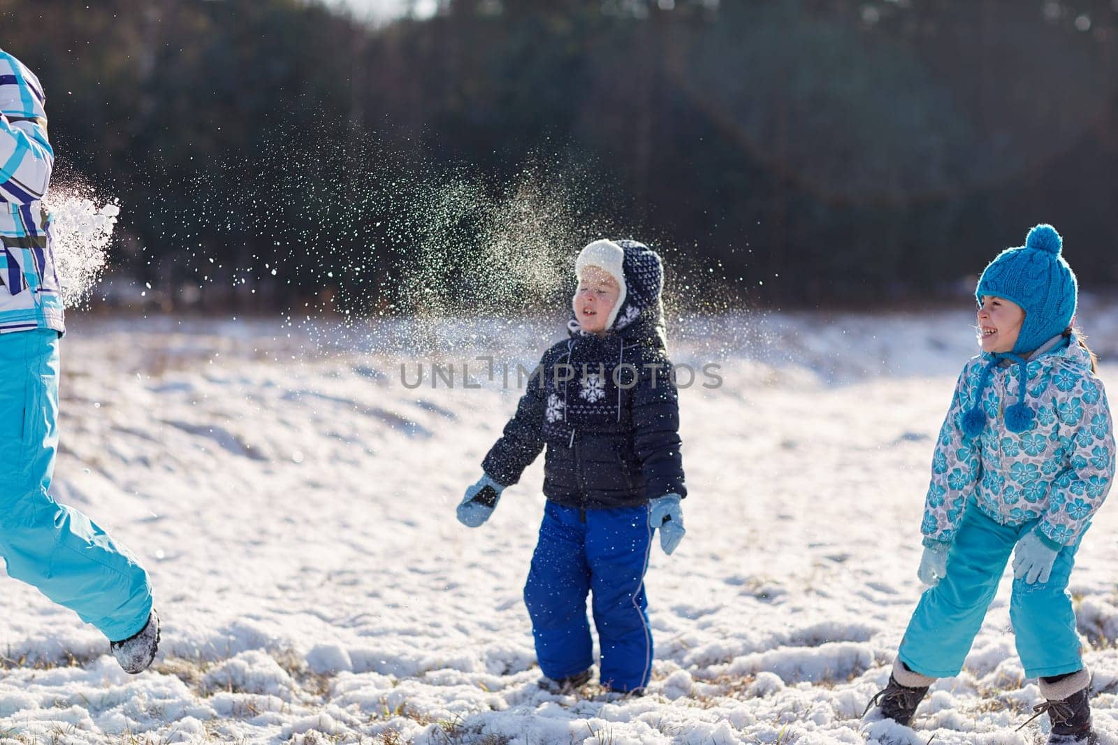 Two kids throwing snowballs at their mother outdoors on a snowy winter's day