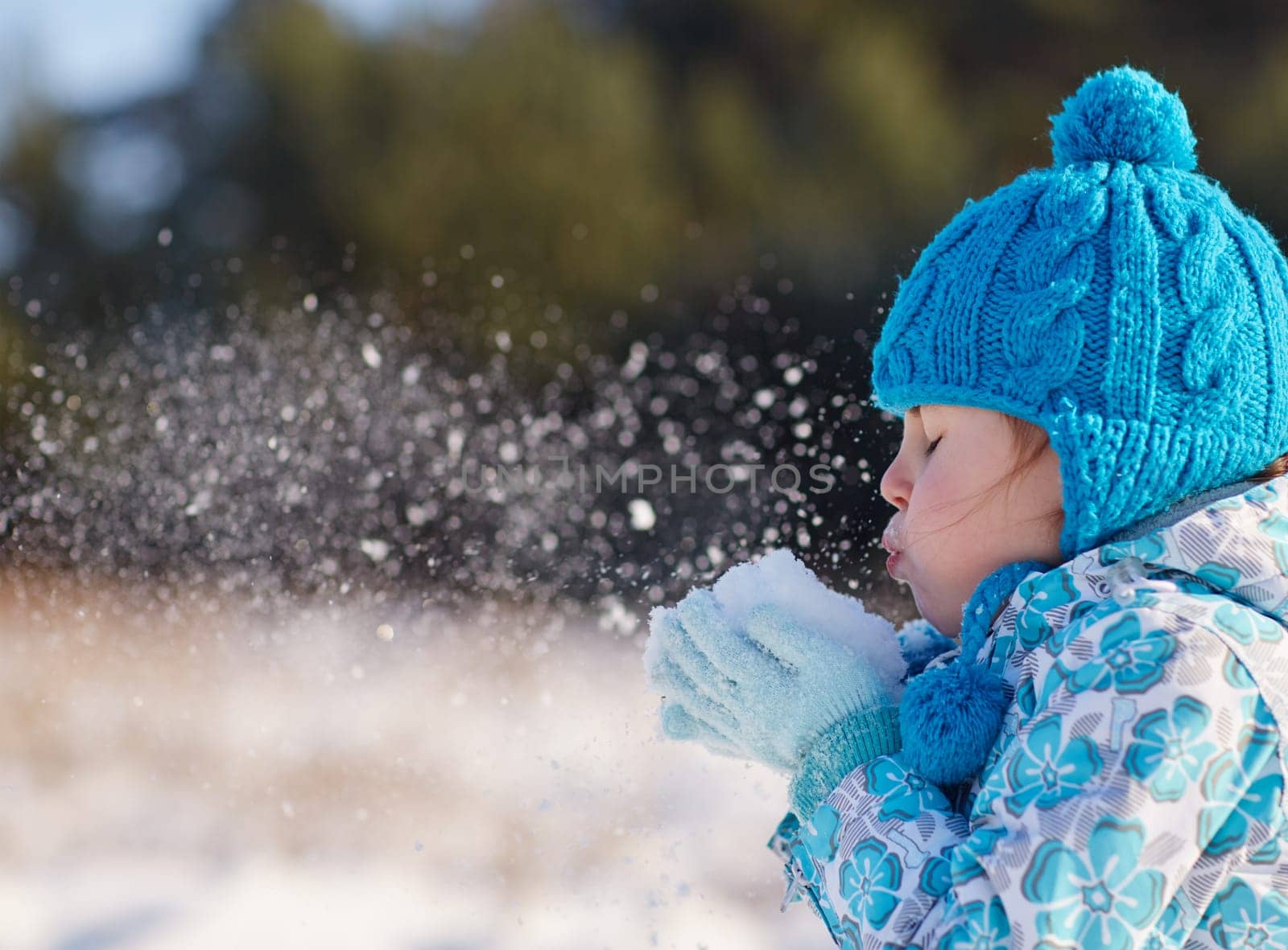 Candid shot of a cute little girl blowing snow flakes from her hands outdoors on a sunny winter's day
