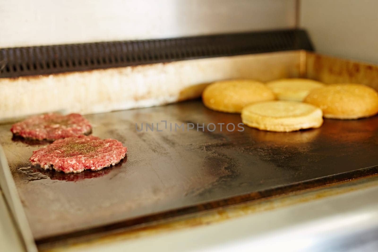 Two burger patties frying next to each other with open buns being toasted nearby.