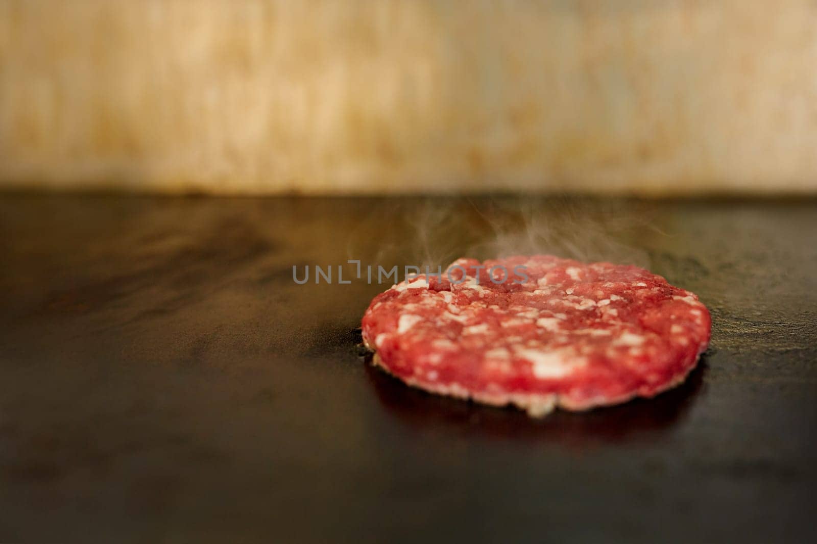 Fresh hamburger patty sizzling on a grill with seasoning on it and steam rising aromatically.