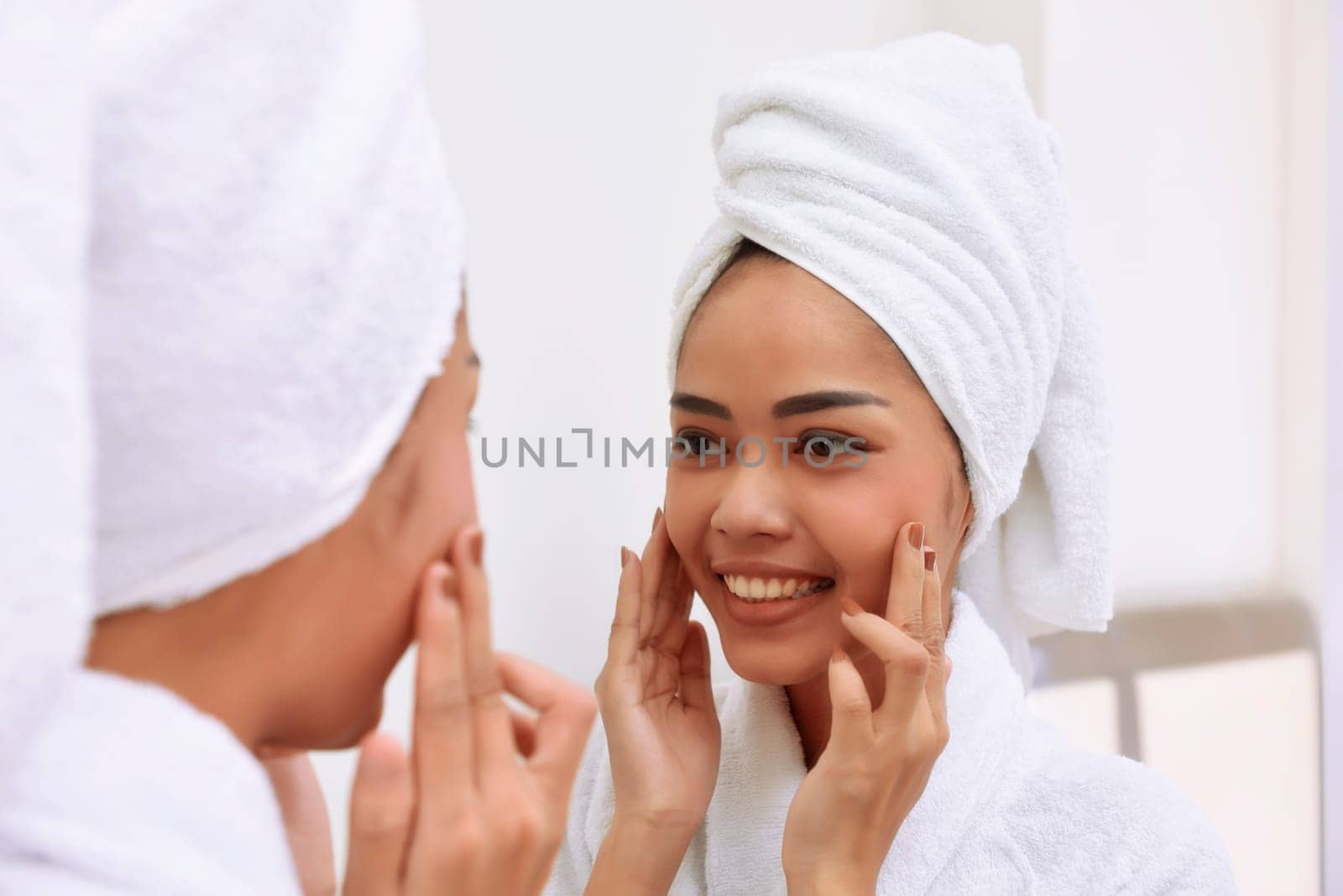 Young asian woman with bath towels cleanses her face at the bathroom