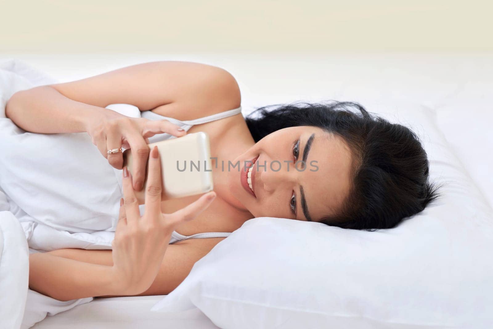 Young asian woman using smartphone while lying in bedroom