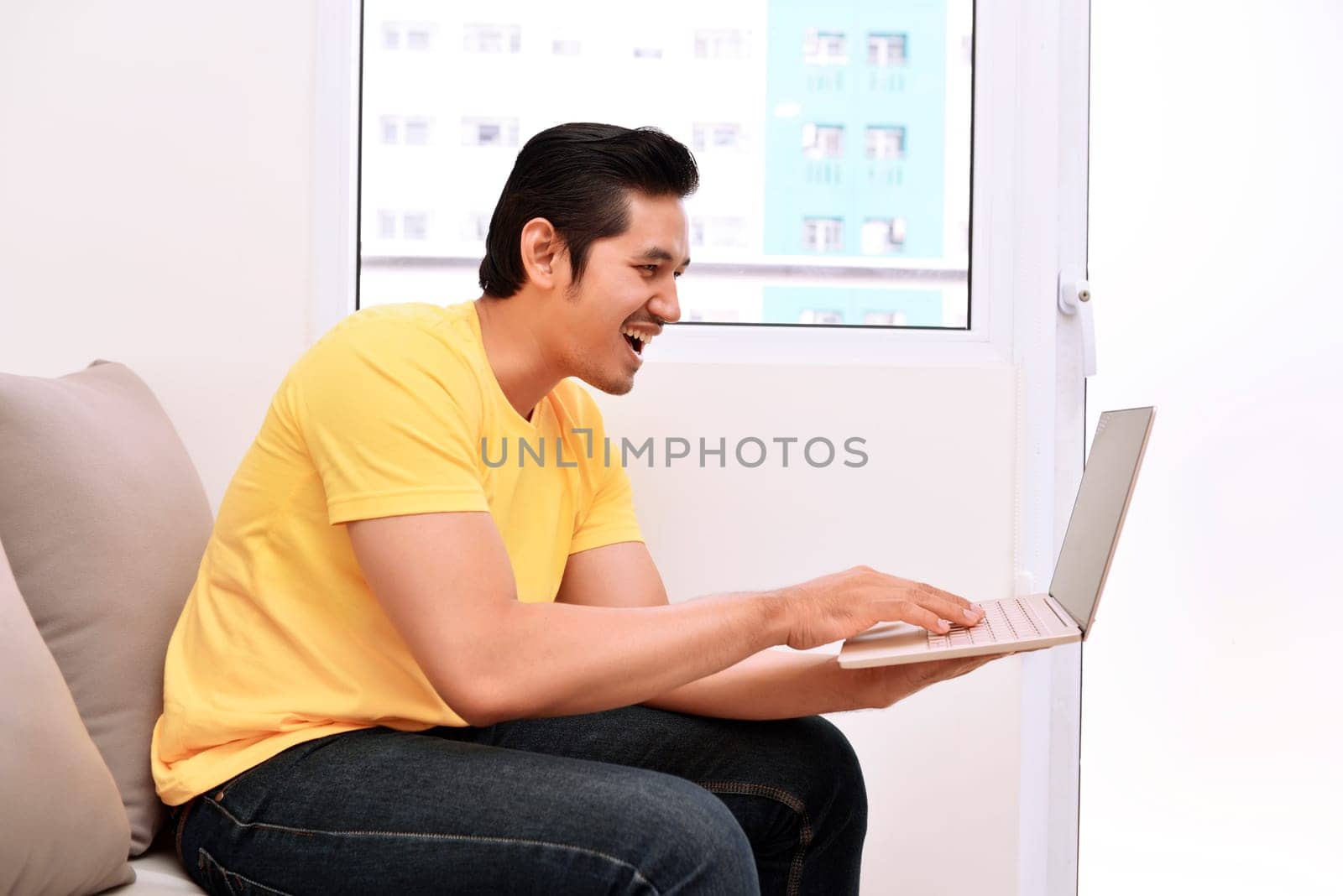 Happy asian man with laptop sitting on the couch at home