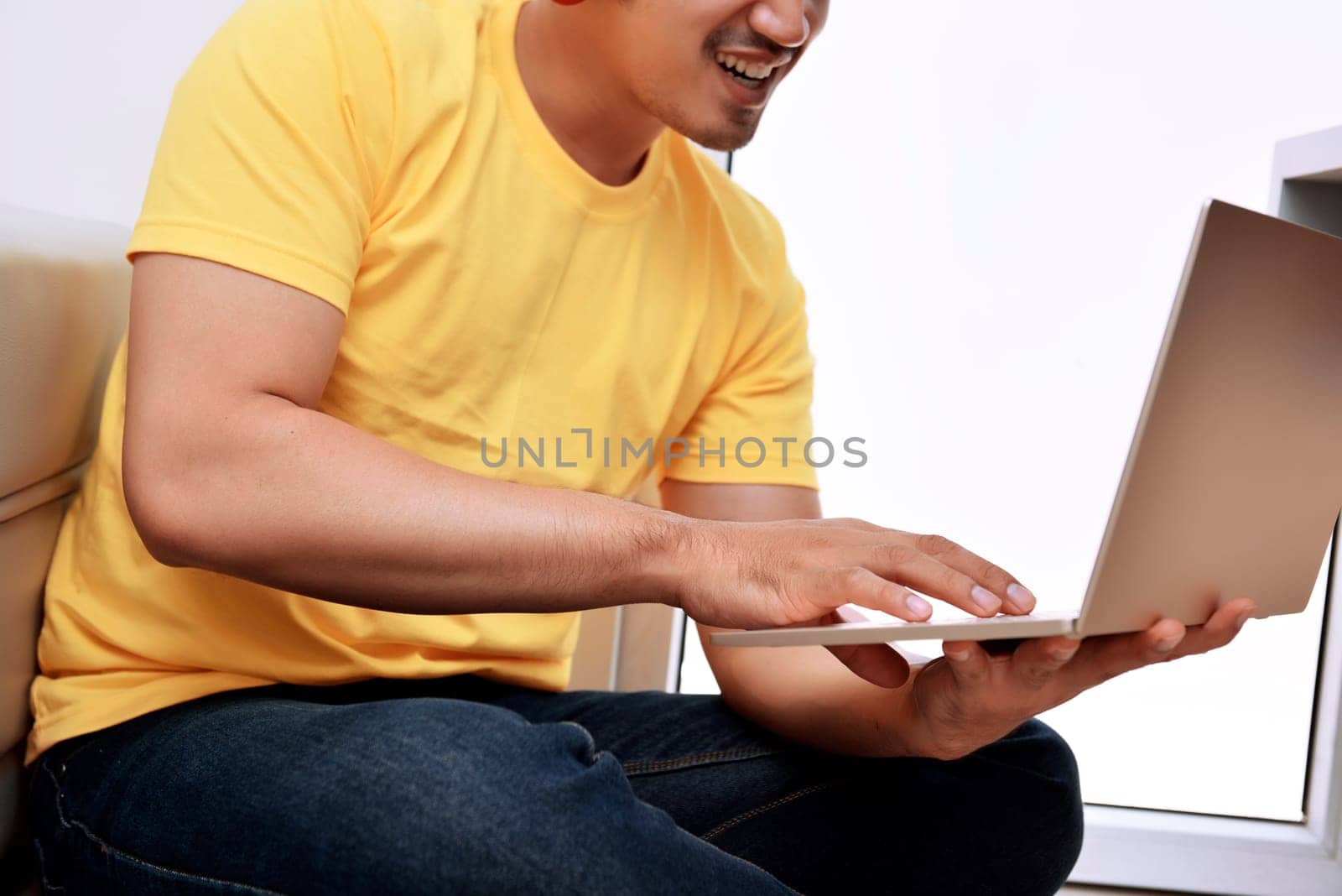 Happy asian man with laptop sitting on the couch at home