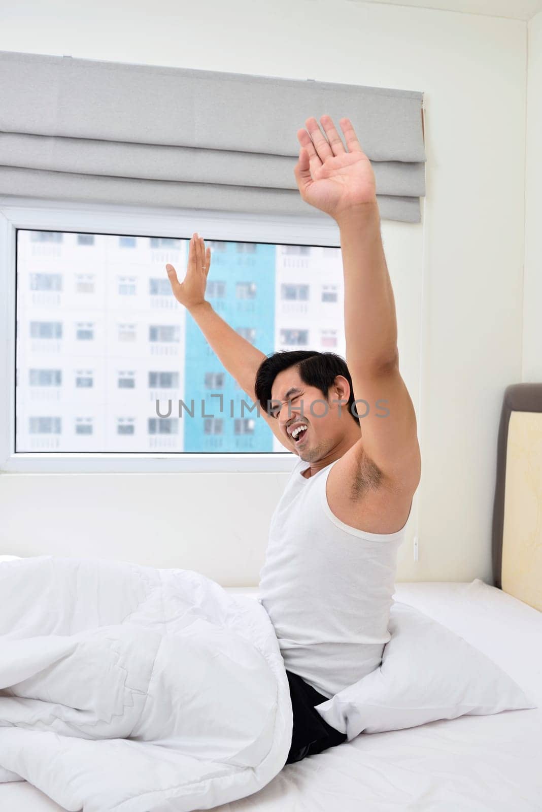 Young asian man waking up and stretching his arms in the morning