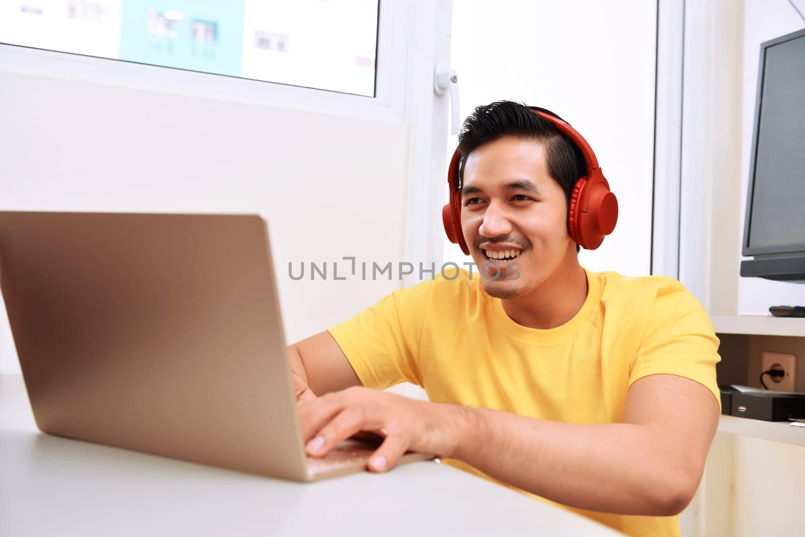 Happy asian man sitting with laptop and headphones in the living room