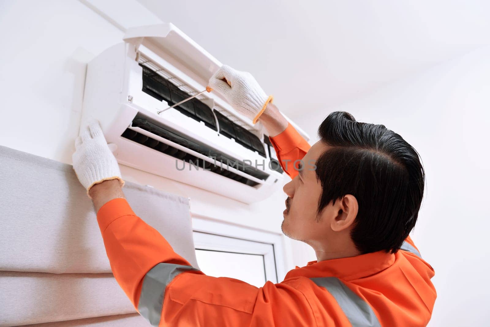 Young asian male technician repairing air conditioner with screwdriver at home