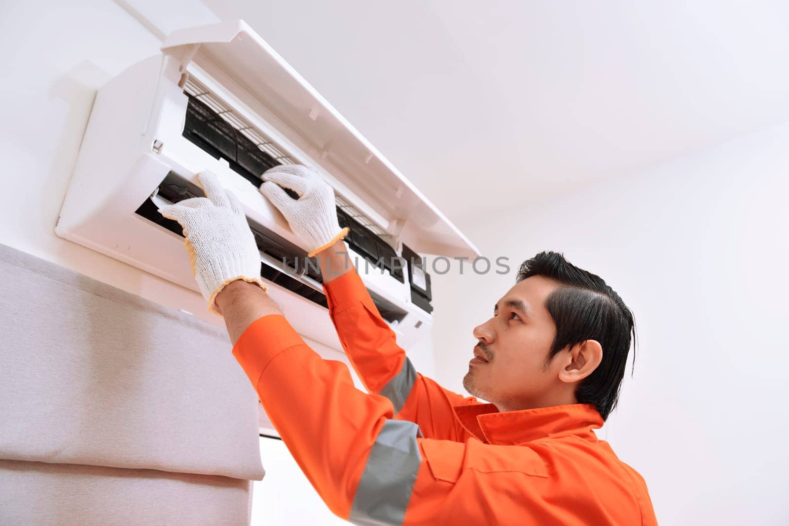 Young asian male technician repairing air conditioner at home
