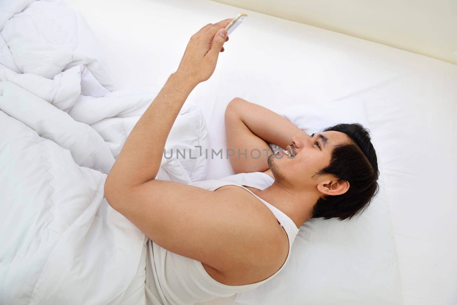 Handsome asian man using cellphone while lying in bedroom