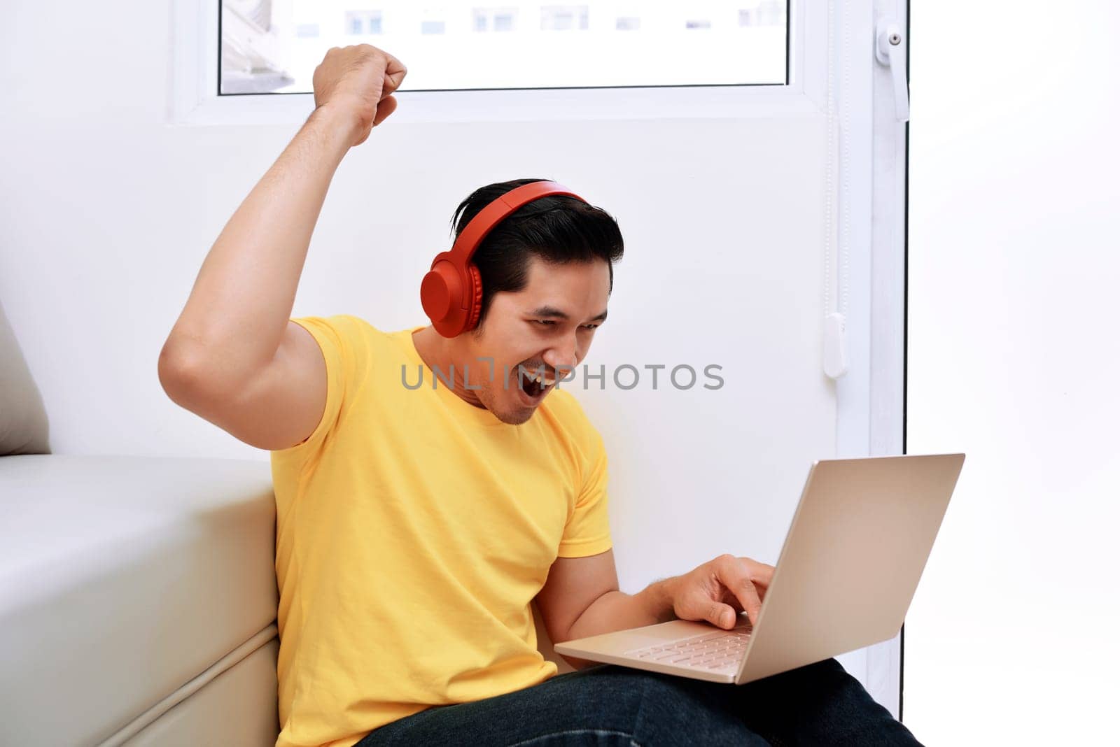 Happy asian man sitting with laptop and headphones in the living room