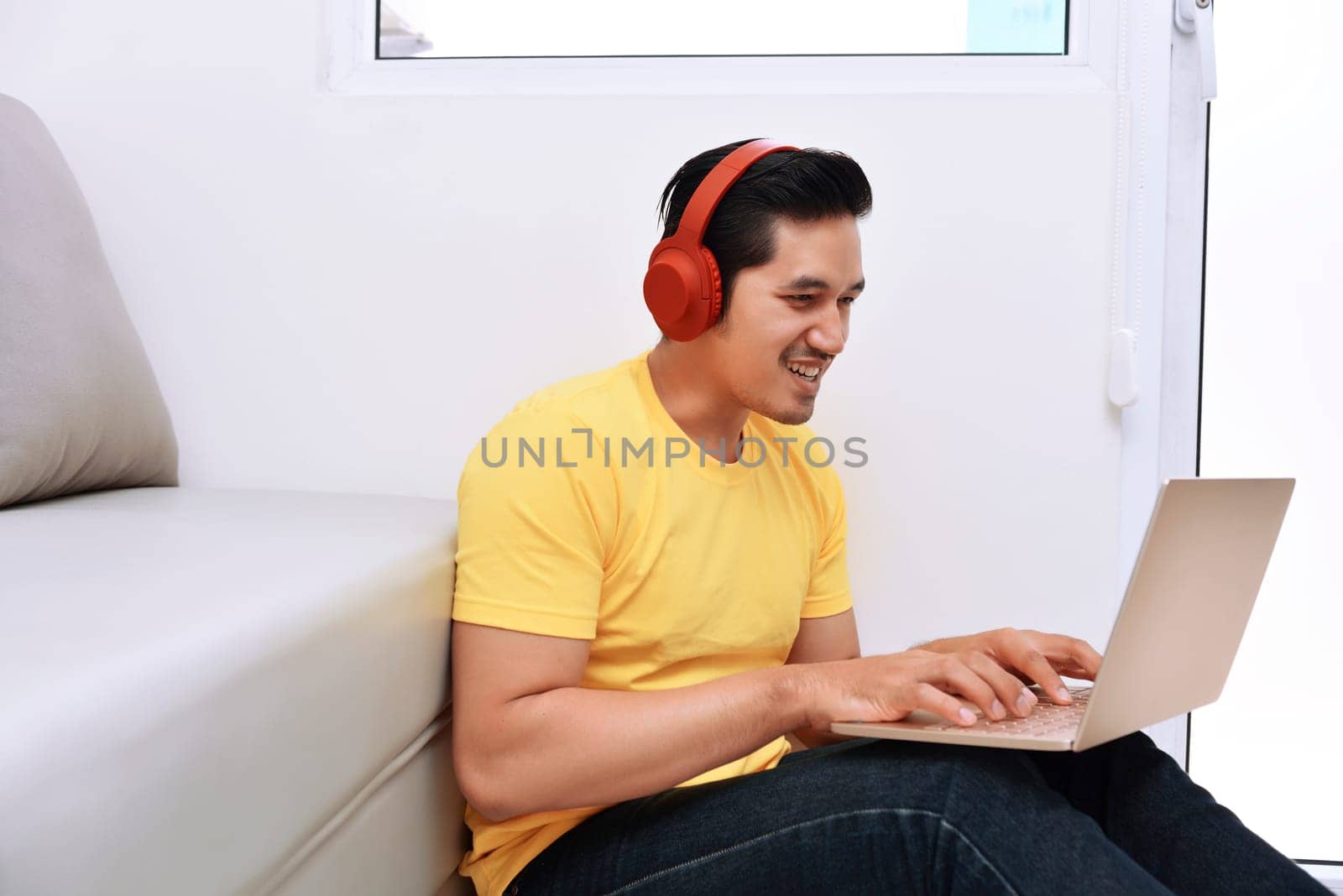 Happy asian man sitting with laptop and headphones in the living room