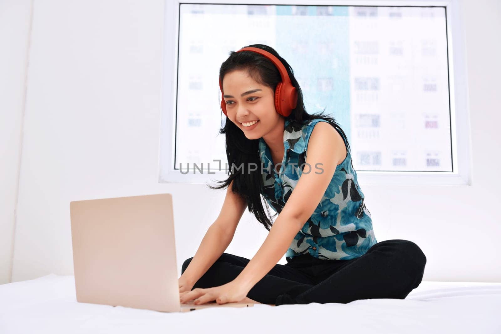 Happy asian woman using laptop and enjoying the music on bedroom