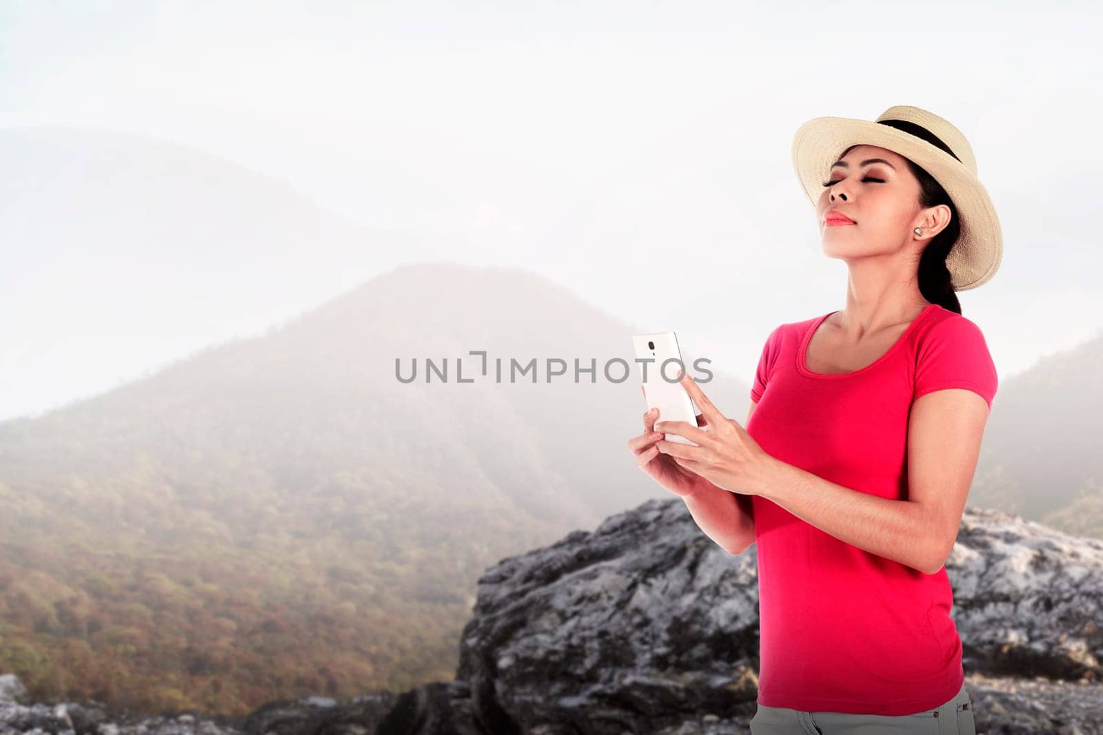 Asian tourist wearing hat holding cellphone at the mountain