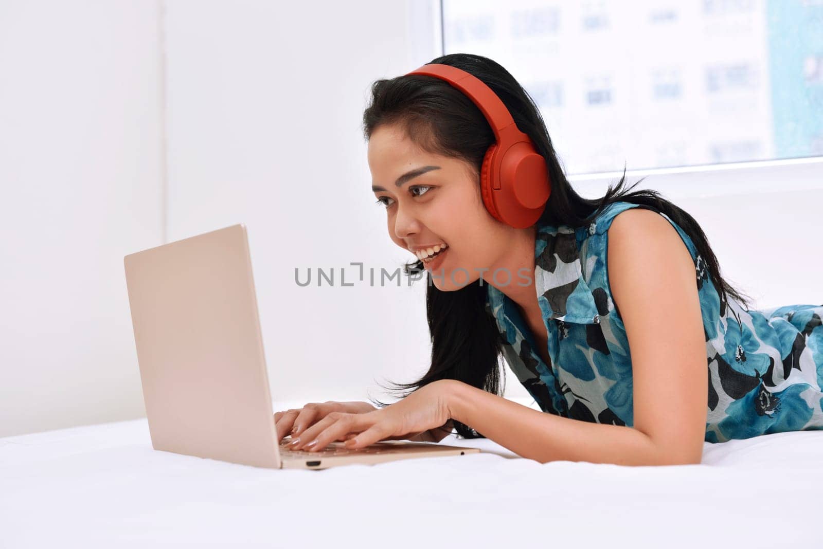 Happy asian woman using laptop and enjoying the music while lying on bedroom